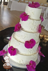 5-tier cake with smooth white icing and decorated with white buttercream scrolls and fresh flowers.