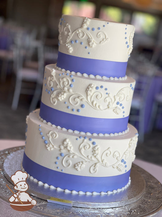 3-tier cake with smooth white icing and white buttercream scrolls and a purple ribbon on the base of each tier.