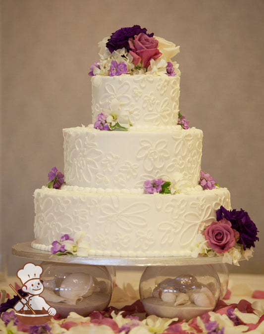 3-tier cake with smooth white icing and decorated with hand-piped white buttercream flowers and a white beaded buttercream trim.