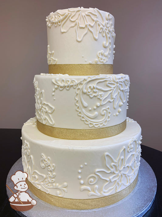 3-tier cake with smooth white icing and decorated with hand-piped white buttercream flowers and a gold shimmery ribbon on the base of each tier.