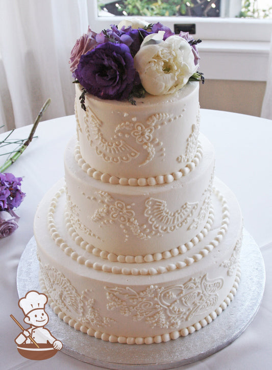 3-tier cake with smooth white icing and decorated with white buttercream piping's and white buttercream beaded trims and fresh flowers on top.