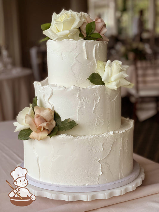 3-tier cake with white icing and a light-texture and fresh flowers in white and cream colors.