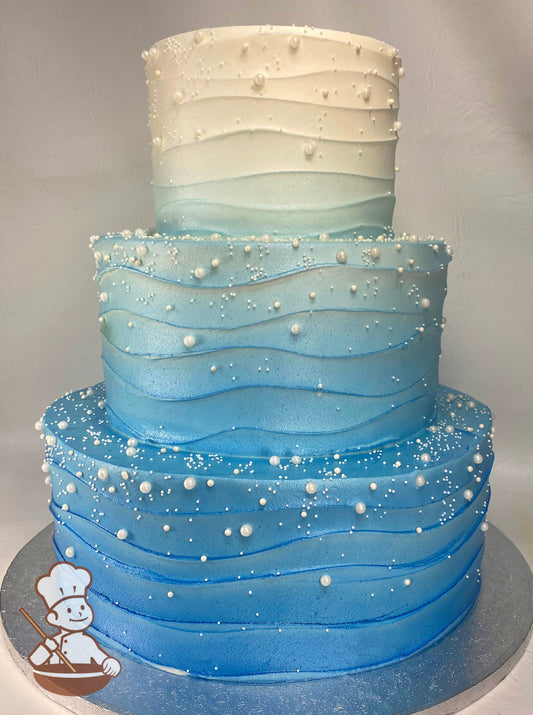 3 tier wedding cake with wavy texture and blue ombre spray and finished with assorted sizes of sugar pearl beads.
