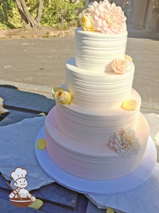 4 tier round buttercream wedding cake with round pattern and coral ombre spray decorated with fresh flowers and petals.