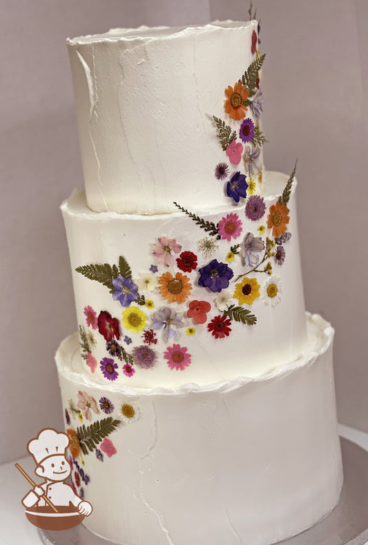 3 tier round textured buttercream wedding cake with top ridges and decorated with cascading dried pressed flowers.