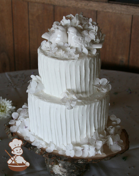 2-tier cake with white icing decorated with a vertical texture and small thin white flowers.