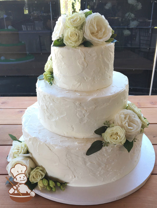 3-tier cake with white icing and decorated with a stucco-like texture and white and cream colored fresh flowers.