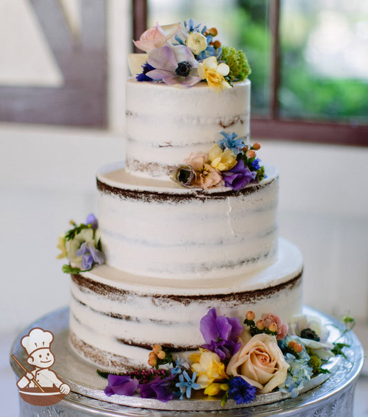 3-tier cake with white icing and decorated with a scraped texture to show some of the cake and fresh flowers.