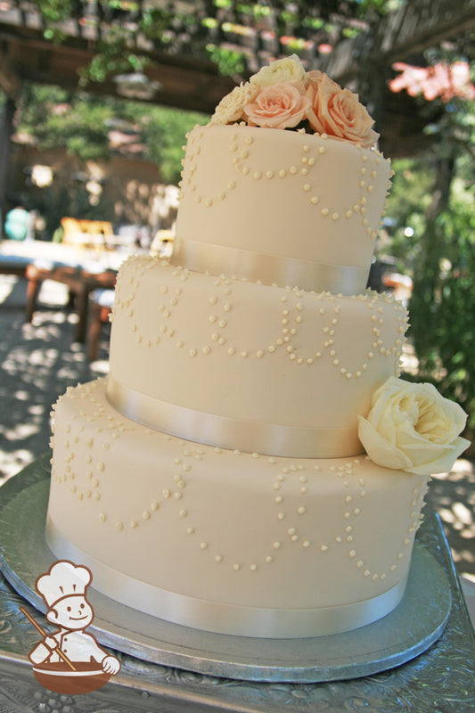 3 tier ivory fondant wedding cake wrapped with ivory satin ribbon and decorated with buttercream bead loop piping and fresh flower decoration.