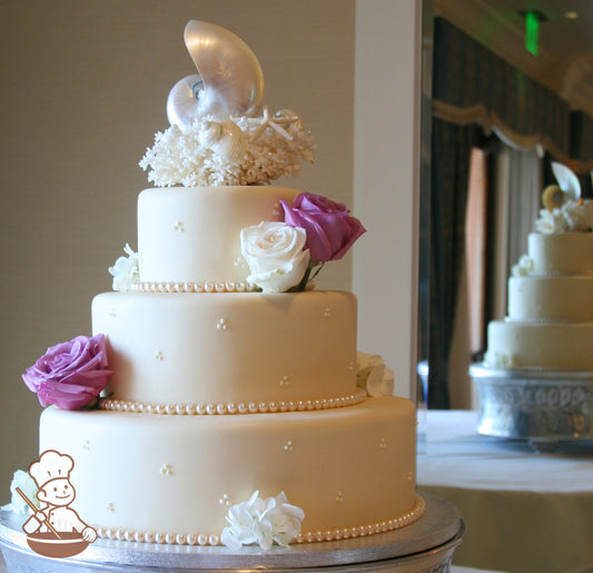 3 tier ivory fondant wedding cake with cream glass pearl bead strands on base of each tier & decorated with fresh flowers.