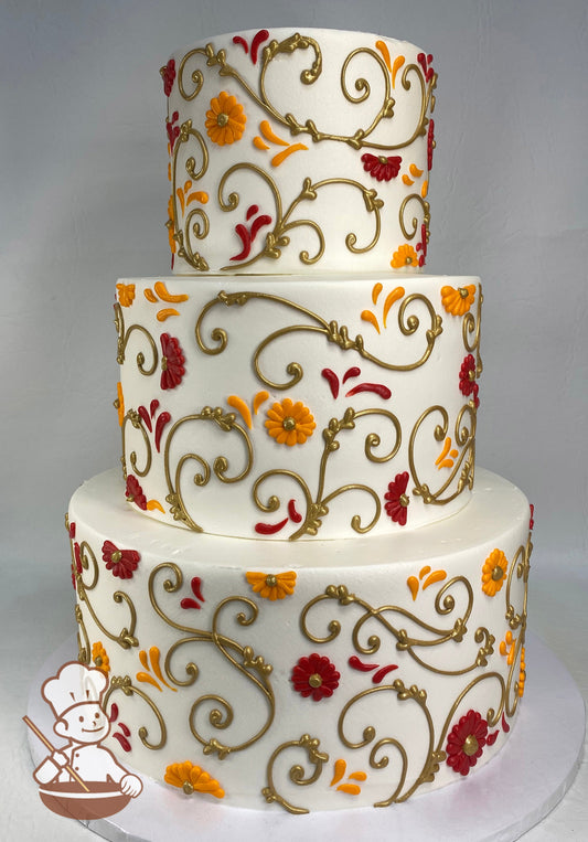 3-tier cake with smooth white icing and decorated with metallic gold scrolls and orange and red buttercream gerbera daisies.