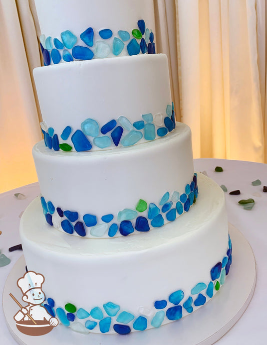 4-tier cake with blue shades of sea glass mosaic decorating the bottom portion of all cake tiers.