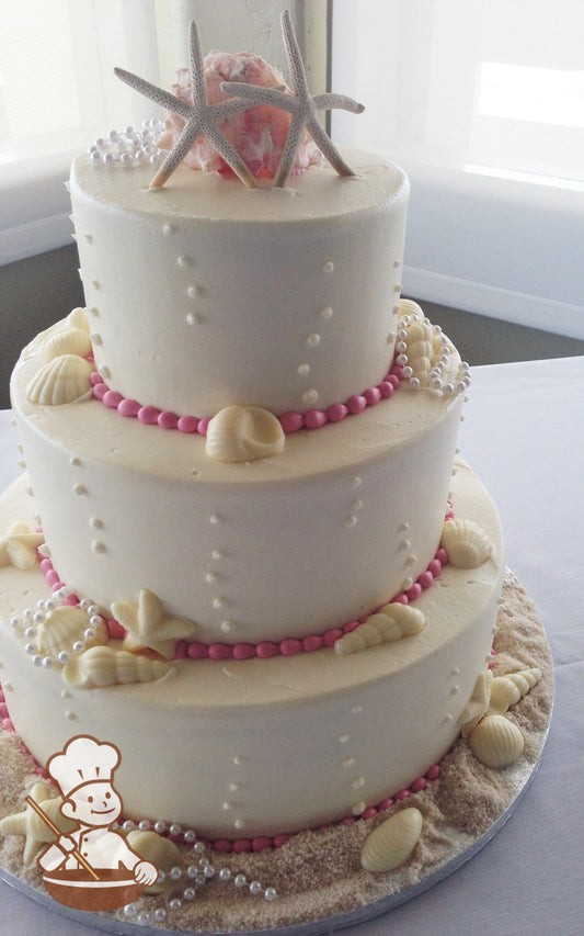 3-tier cake with ocean bubbles and seashells decorated. Cake base has brown sugar sand.