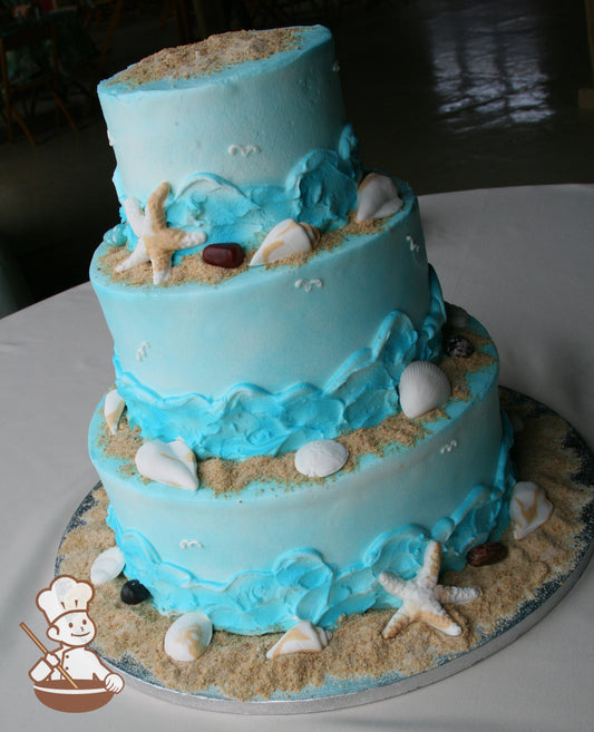 3-tier blue cake with piped blue waves and sea gulls, brown sugar sand, and sea shells.