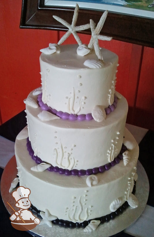 3-tier white cake with piped kelps and bubbles and decorated with sea shells. Cake trim colors go from dark purple to lavendar.