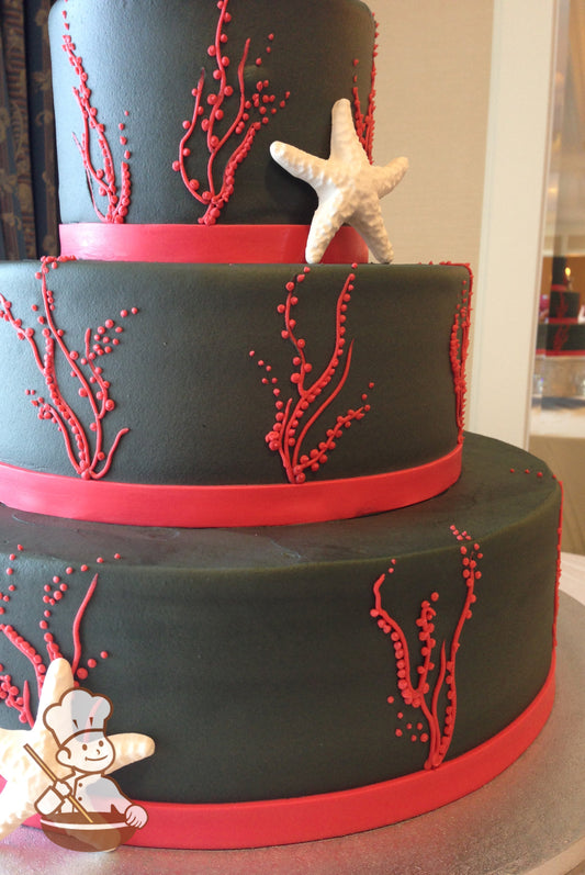 Black 3-tier cake with piped red corals and red band. Decorated with Starfish.