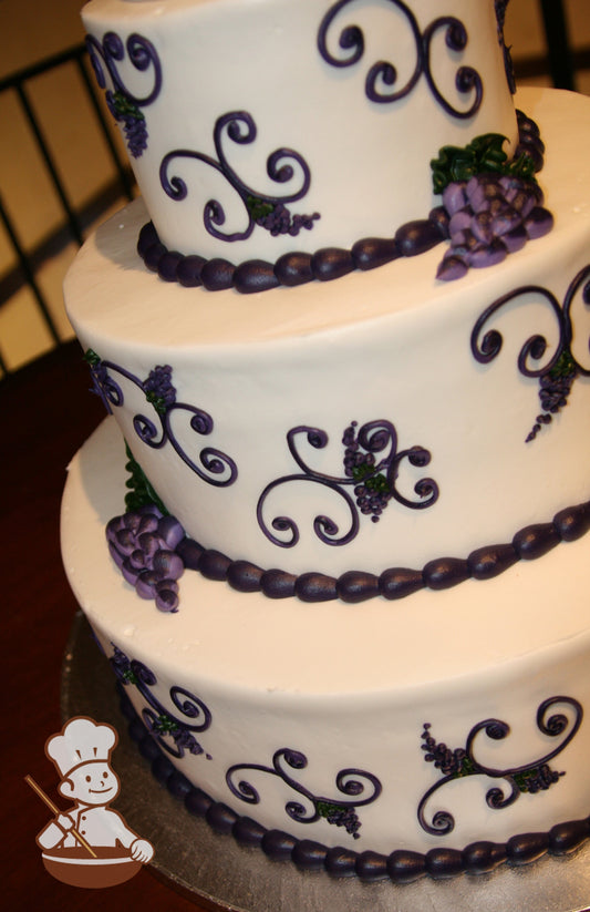 3-tier cake with hand piped scrolls with vineyard details and clusters of hand piped grapes. The cake is white with purple color details.
