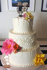 3-tier cake with smooth white icing and decorated with white buttercream dot-loop piping on the bottom tier and buttercream flowers in middle.