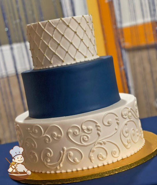 Cake with white icing and buttercream scrolls on the bottom tier, a blue smooth icing in middle tier and a piped white quilt pattern on top tier.