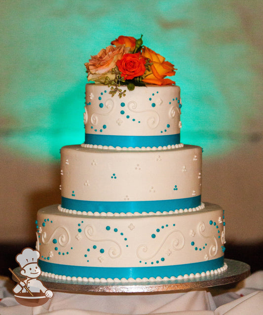3-tier cake with smooth white icing and decorated with white buttercream scrolls, white and turquoise buttercream dots and a turquoise ribbon.