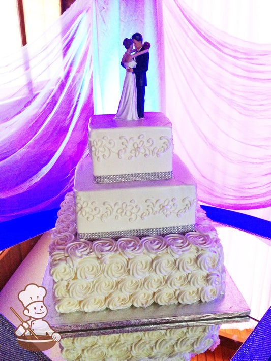 3 tier square wedding cake with rosette swirls and floral themed piping wrapped with crystal band & finished with traditionl figurine topper.