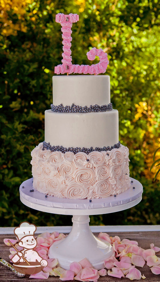 3 tier round wedding cake with light pink rosette swirls and gray fondant pearl bands and finished with a floral monogram topper.