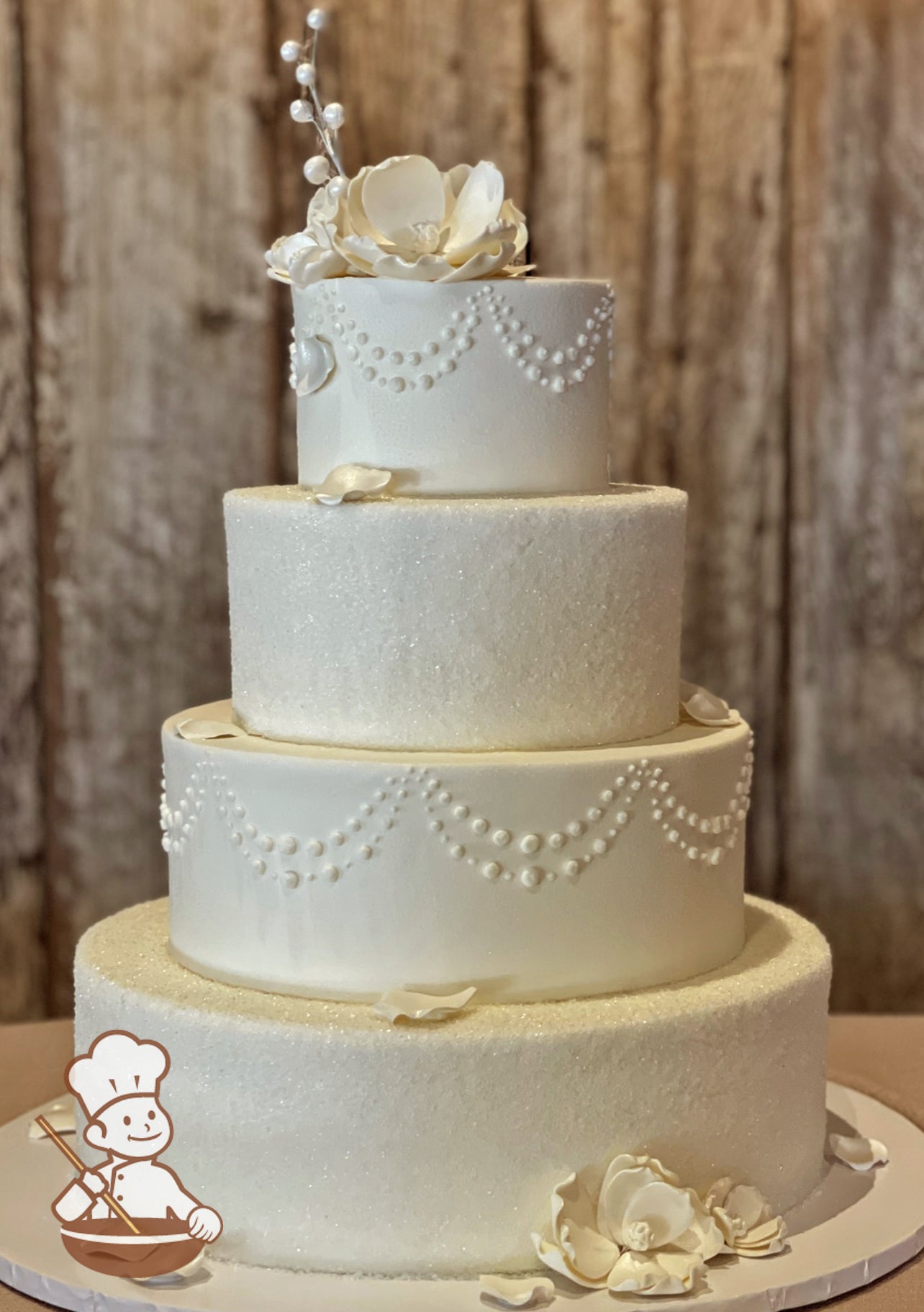 4 Tier round wedding cake with sugar crystals and bead pipings in alternating tiers. Cake is finished with pearlescent sugar flowers and petals.