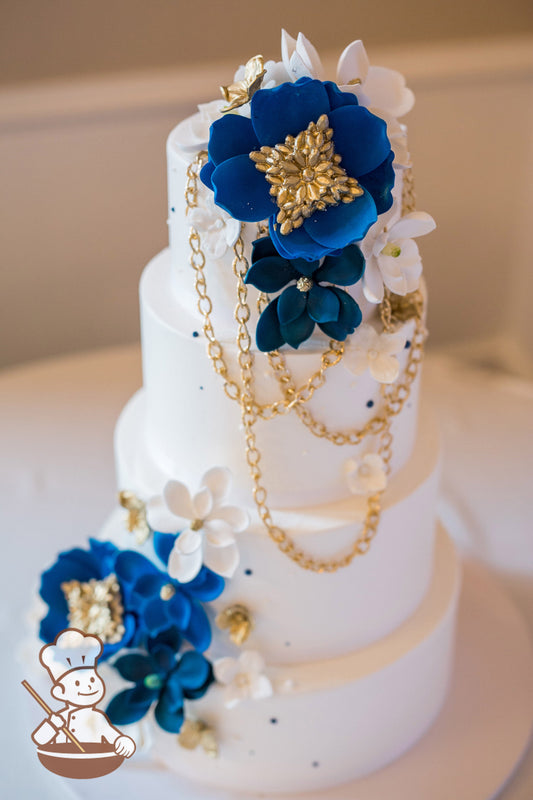 4 tier round buttercream wedding cake with blue & white sugar flowers and gold necklace & broach decor along with touches of blue piping.