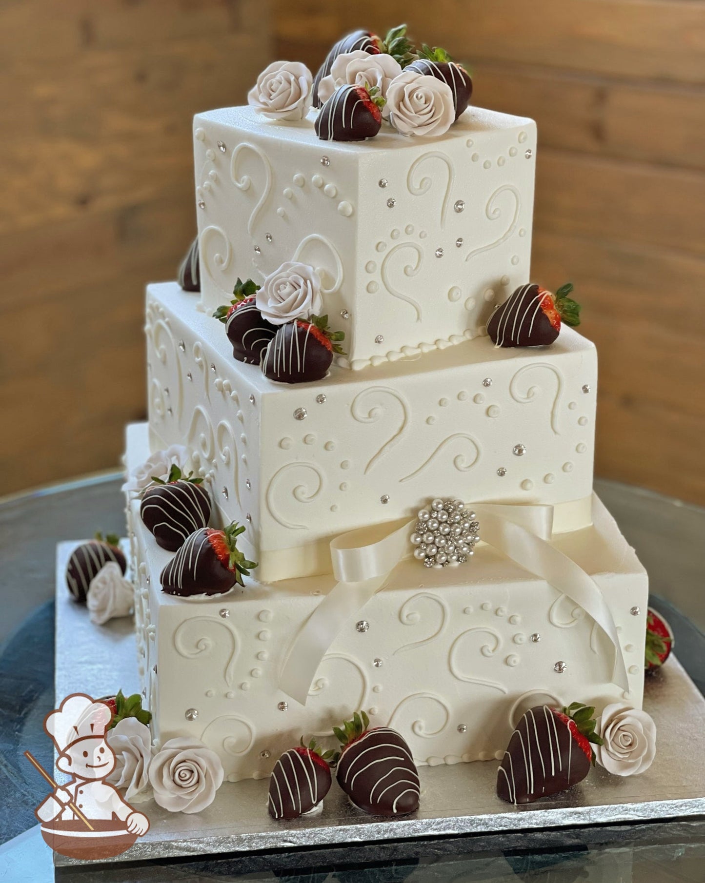 3 tier square offset wedding cake with chocolate dipped strawberries and sugar flowers. Cake is finished with traditional piping and rhinestone.