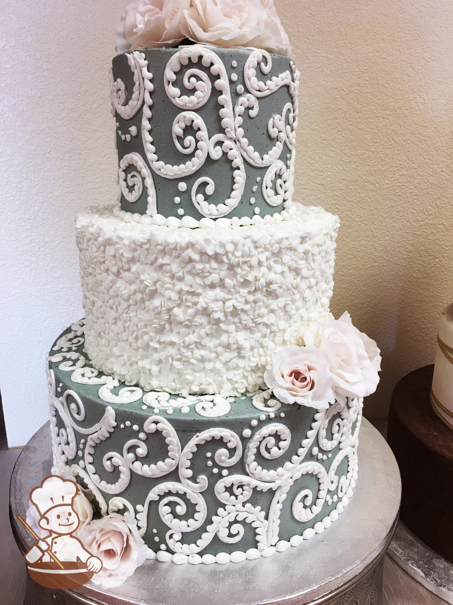 3 tier round wedding cake with gray icing and white vintage piping. Middle tier is covered with white sprinkle texture.