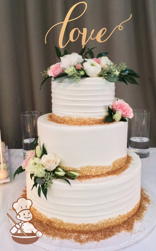 3-tier cake with white icing and decorated with a horizontal texture on the bottom and top tier and gold sanding sugar on the base of each tier.