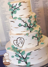 4-tier cake with smooth white icing and decorated with a painted wood grain look and a heart with the initials G + G.