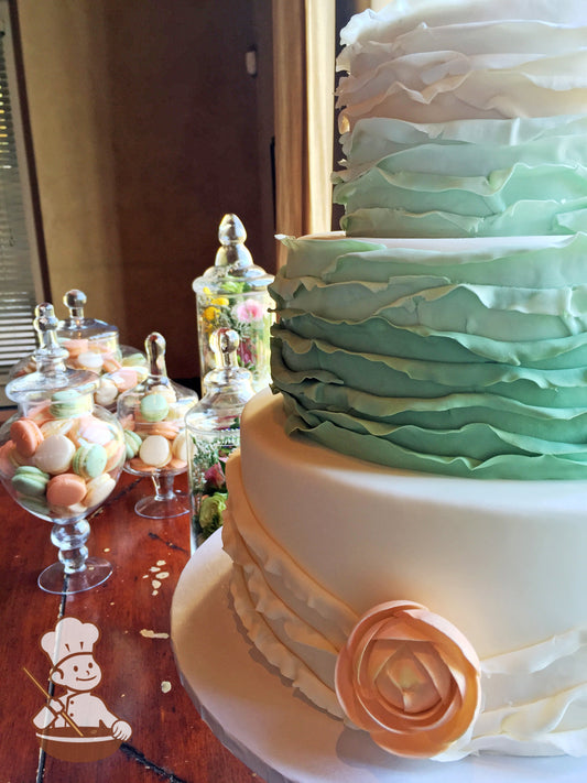 3 tier wedding cake with sage green to cream ombre fondant ruffle wrap and sugar flower center.