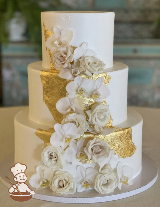 3-tier cake with smooth white icing and decorated with gold sheets cascading in front of the cake.