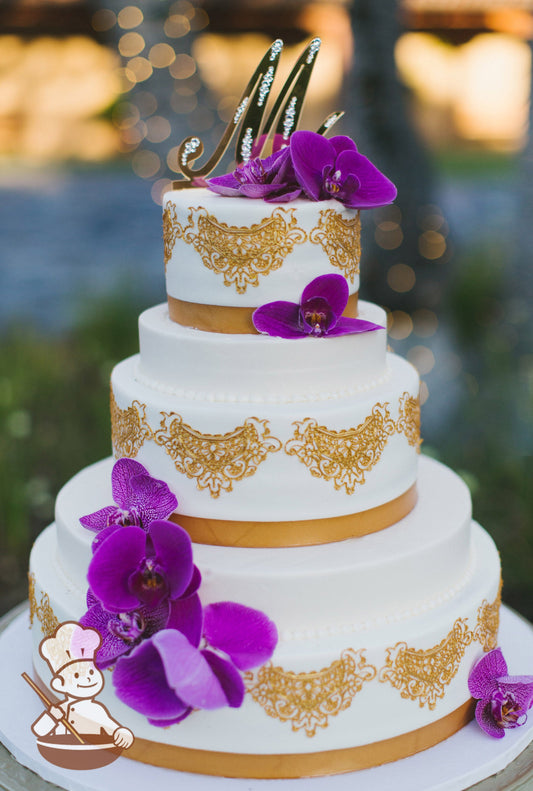 Cake with smooth white icing and decorated with a gold lace draping and gold ribbon with orchid flowers.