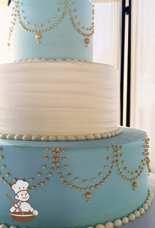 3-tier cake with dusty-blue icing and metallic gold pipings on the bottom and top tier and white icing with horizontal texture in the middle.