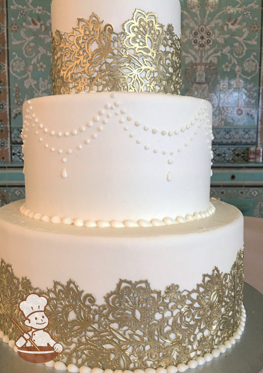 3-tier cake with smooth white icing and decorated with a gold lace on the bottom and top tier and white buttercream pipings in the middle tier.