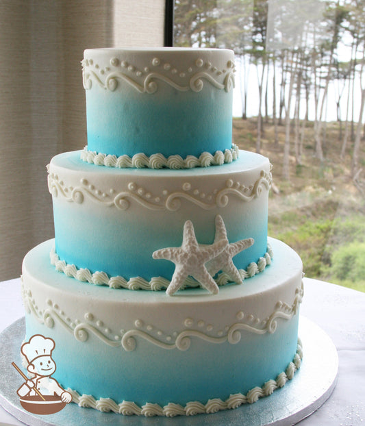 3-tier cake with smooth white icing and decorated with an airbrushed ombre blue coloring and white buttercream wave scrolls.