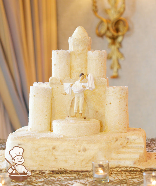 Cake decorated to look like a sandcastle by being coated with sugar "sand" and sugar crystals with a plastic topper of a couple getting married.