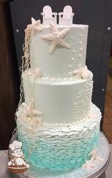 3-tier cake decorated with wavy buttercream piping on the bottom tier and hand-piped buttercream coral on the middle tier, netting and seashells.