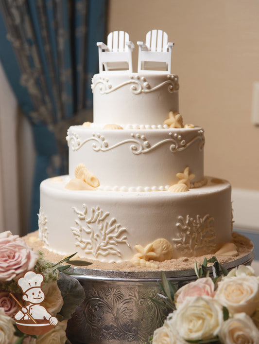 3-tier cake with smooth white icing and decorated with hand-piped white buttercream coral and white chocolate seashells.