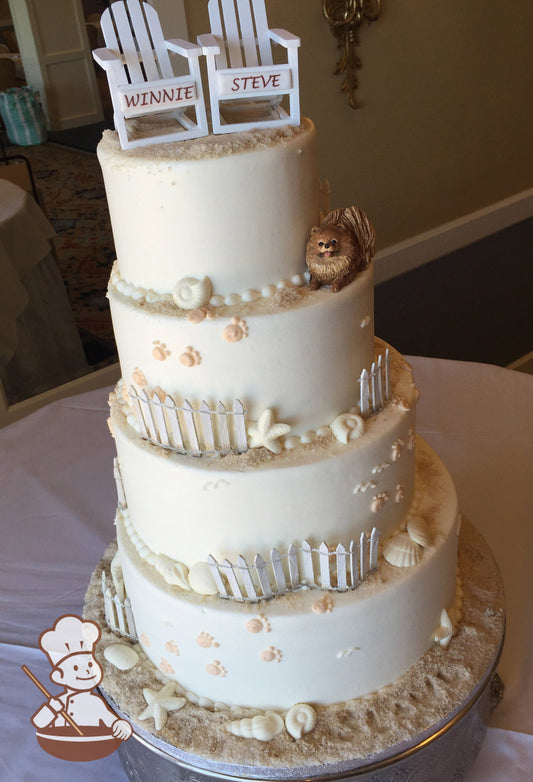 4-tier cake with ivory-colored smooth icing and decorated with white wood fences, white chocolate seashells, buttercream dog paws & sugar "sand".