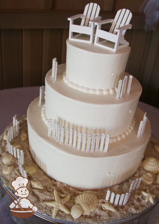 3-tier cake with smooth white icing and decorated with wood white fences, 2 white wood beach chairs, white chocolate seashells and sugar "sand".