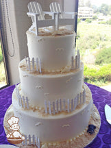 3-tier cake with smooth white icing and decorated with wood white fences, 2 white wood beach chairs, white chocolate seashells and sugar "sand".