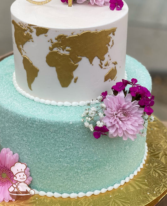 2-tier cake with bottom tier in sea-green color with white sugar crystals. Top tier is iced white with a hand-painted world map in gold.