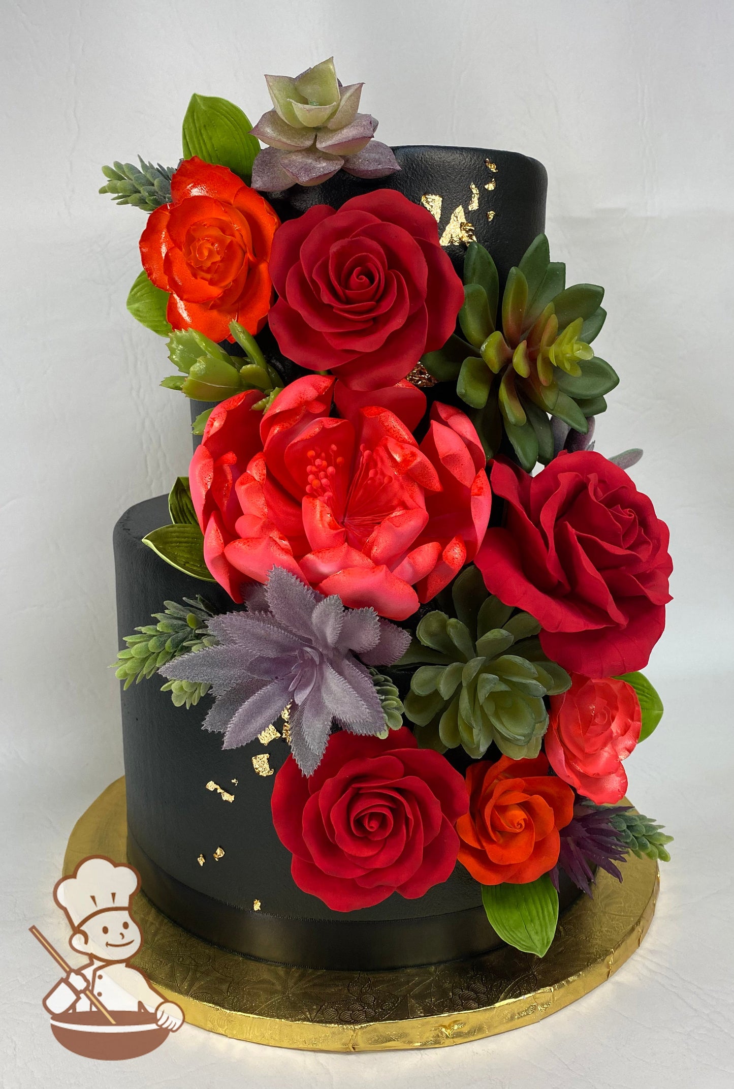 2 tier round wedding cake with black buttercream and decorated with assorted red sugar flowers with gold leaf accent.