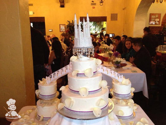 Three sets of cake connected by two staircase leading to a castle. Cake sets are 2, 2, and 3 tiers; all with burgundy and rhinestone bands.