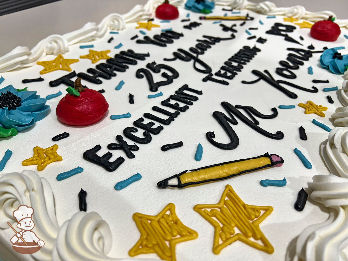 Sheet cake with white buttercream frosting, decorated with red apple designs, blue flowers, yellow stars, a yellow pencil, and blue and black sprinkles.
