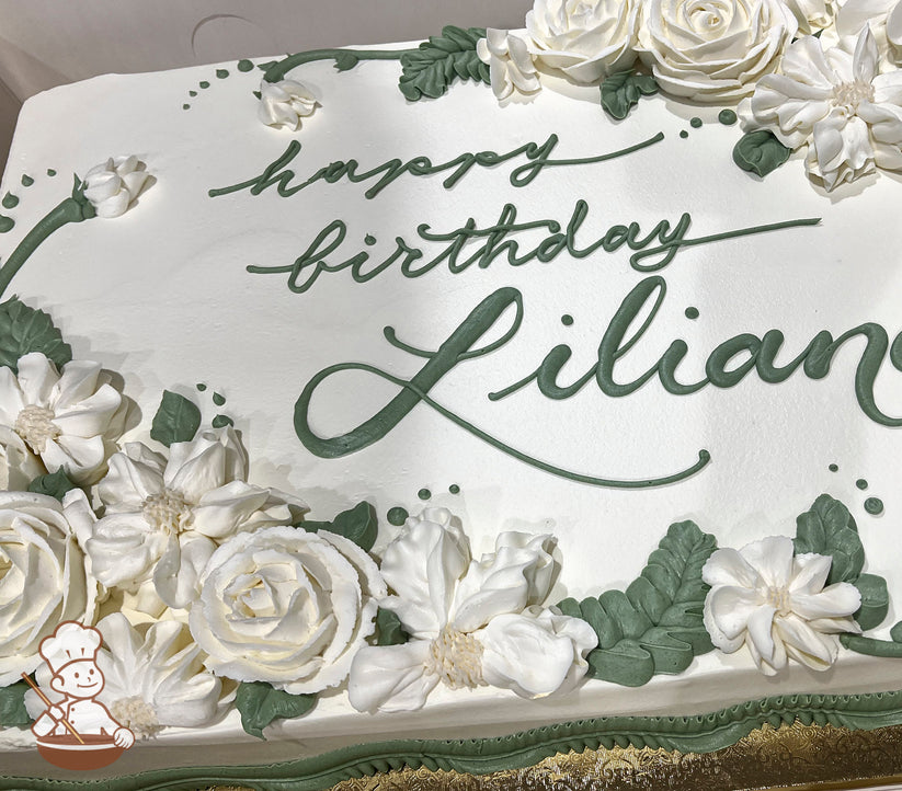 White sheet cake with buttercream roses, blossoms, and green leaves arranged in clusters at the corners and edges, with piped green accents.