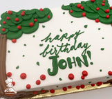 Sheet cake with buttercream apple tree decorations, featuring green leaves, red apples, and brown tree trunks. Red and green accents scattered on white frosting.